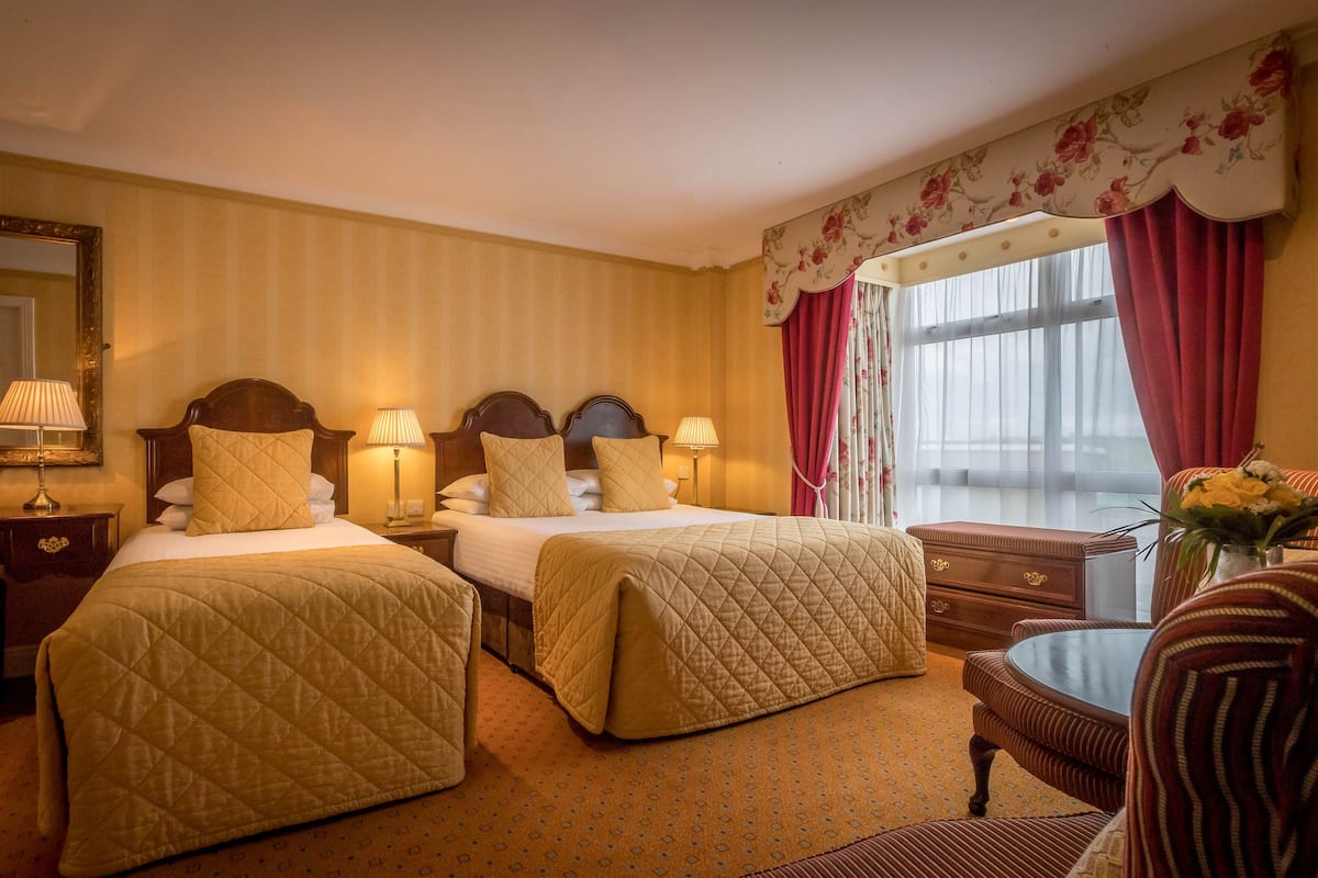 Une chambre d’hôtel avec deux lits, un bureau, une chaise et une fenêtre avec des rideaux.