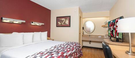 A hotel room with a bed, a desk with a mirror, a television, and a framed picture on the wall.