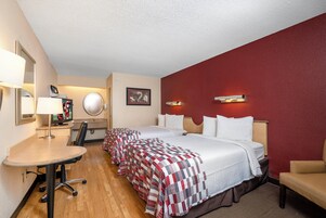A hotel room with two beds, a desk, a chair, a television, and a mirror.