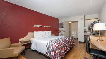 A hotel room with a bed, a desk, a chair, a TV, and a bathroom visible through an open door.