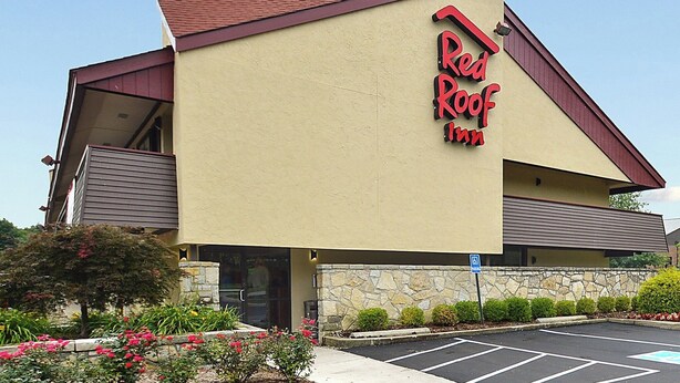 A Red Roof Inn with a stone facade, a parking lot, and a clear sky.
