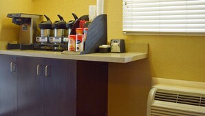 A kitchenette with a coffee machine, a kettle, and a microwave. There are cabinets below and a window with blinds to the right.