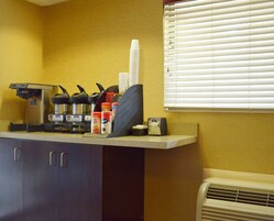A kitchenette with a coffee machine, a kettle, and a microwave. There are cabinets below and a window with blinds to the right.