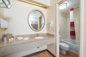 Un baño con lavamanos, espejo, toallero y ducha con cortina a rayas.