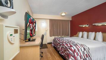 Habitación de hotel con cama, escritorio con televisor, panel de control y una puerta con cortina.