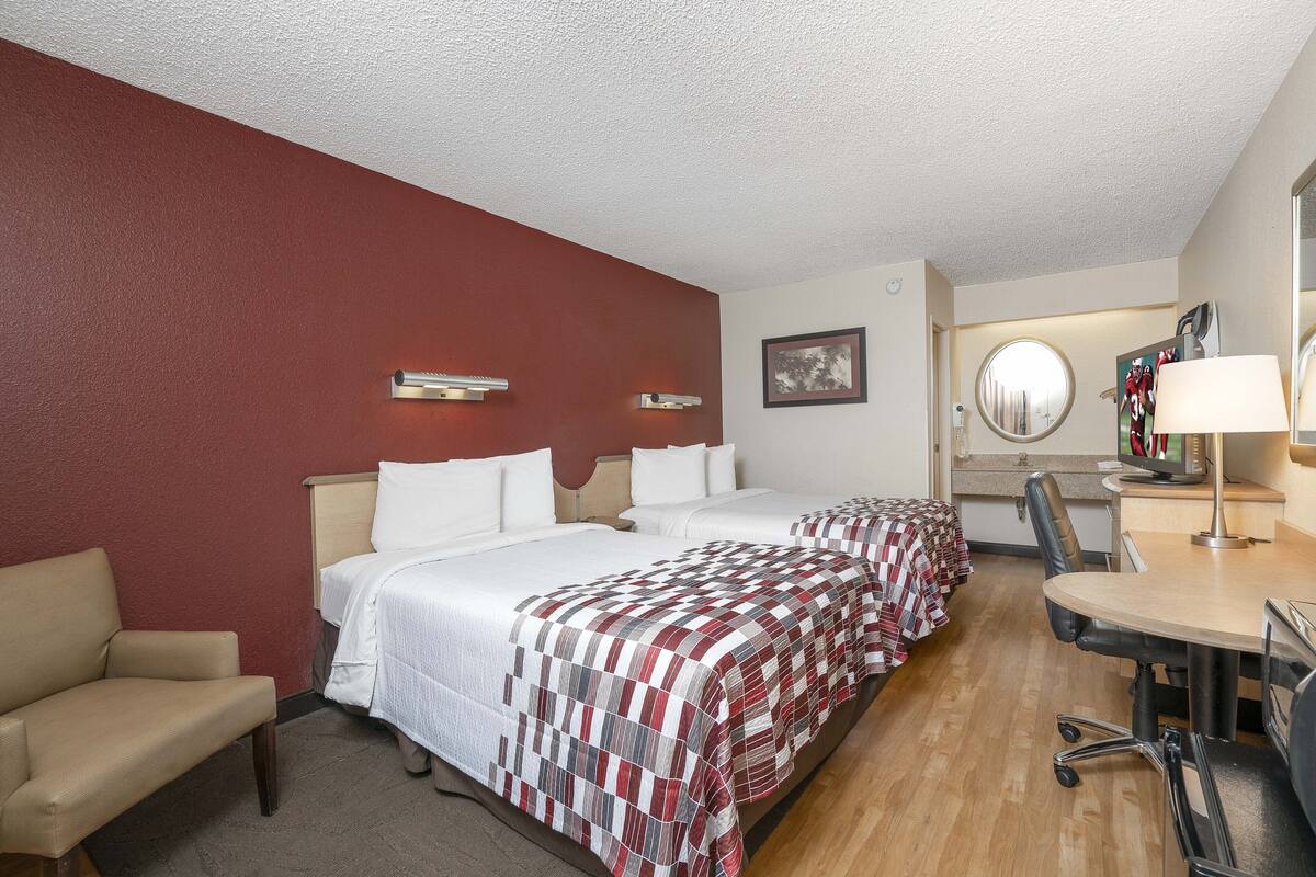 A hotel room with two beds, a desk, a chair, and a small sofa.