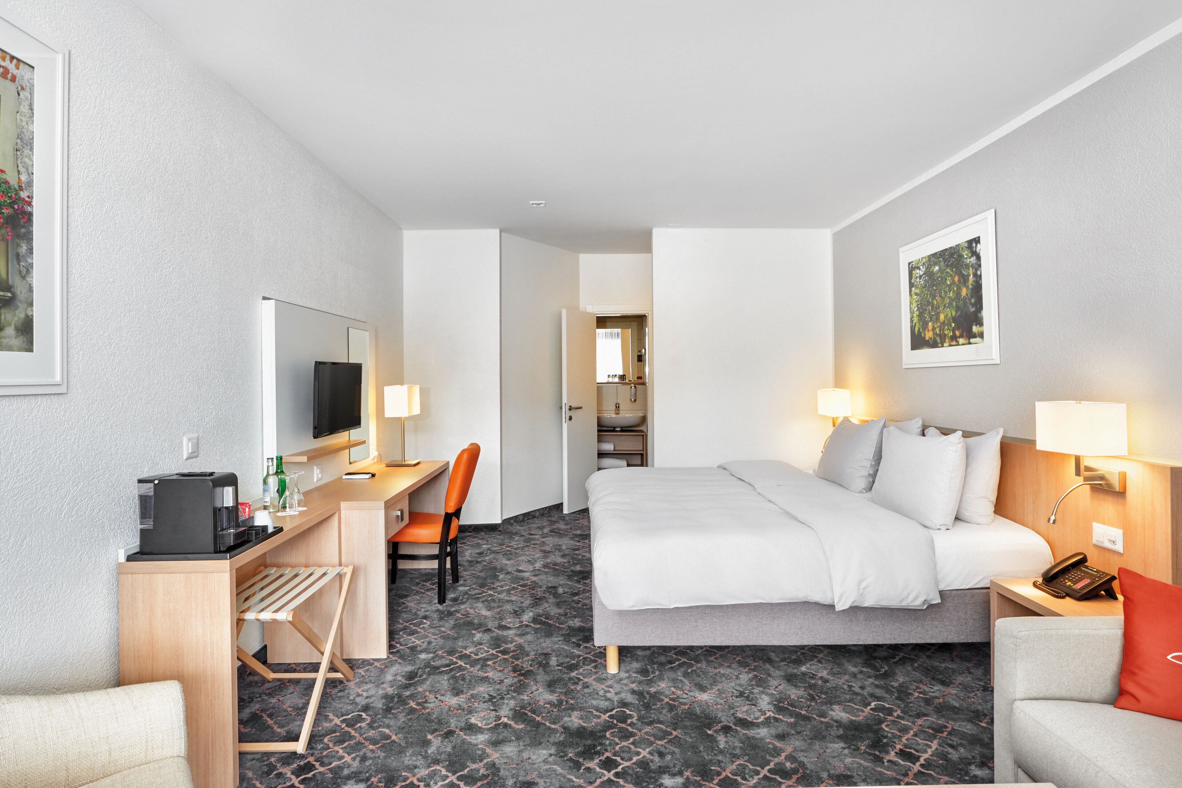 A hotel room with a bed, desk, chair, and a small kitchenette area.