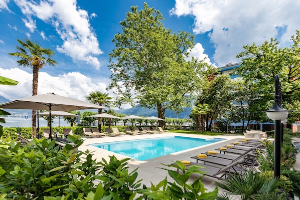 Una piscina al aire libre, sombrillas, sillones reclinables de piscina