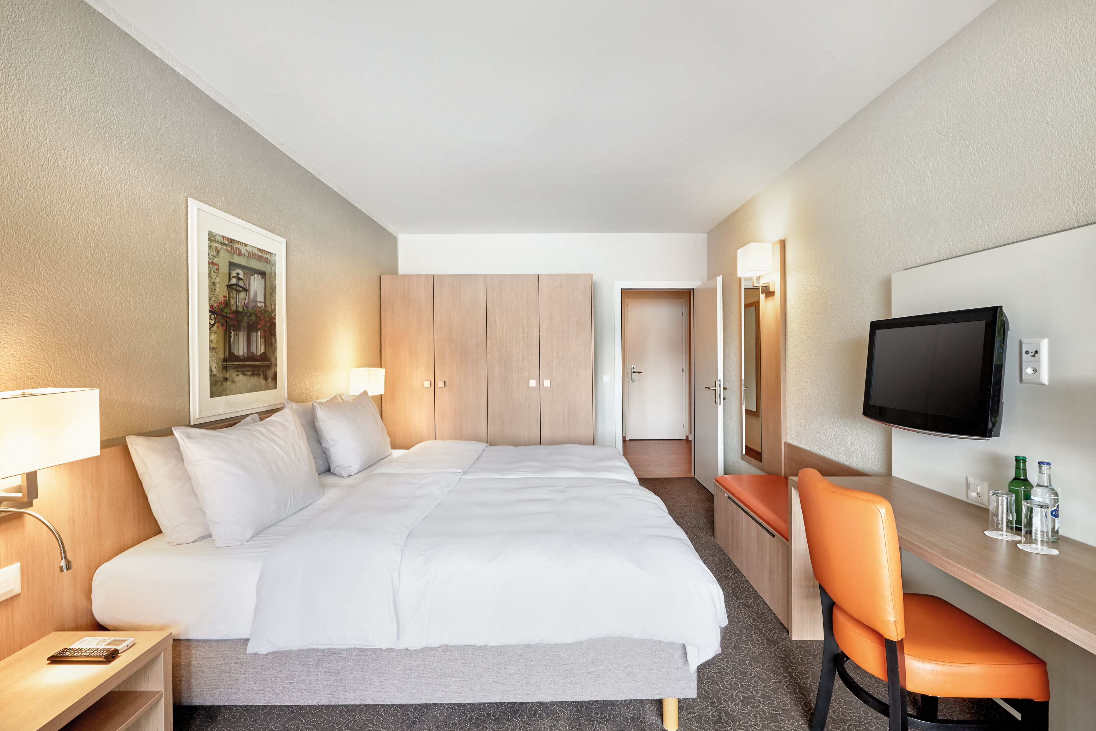 Een hotelkamer met een bed, een bureau, een stoel, een televisie en een schilderij aan de muur.