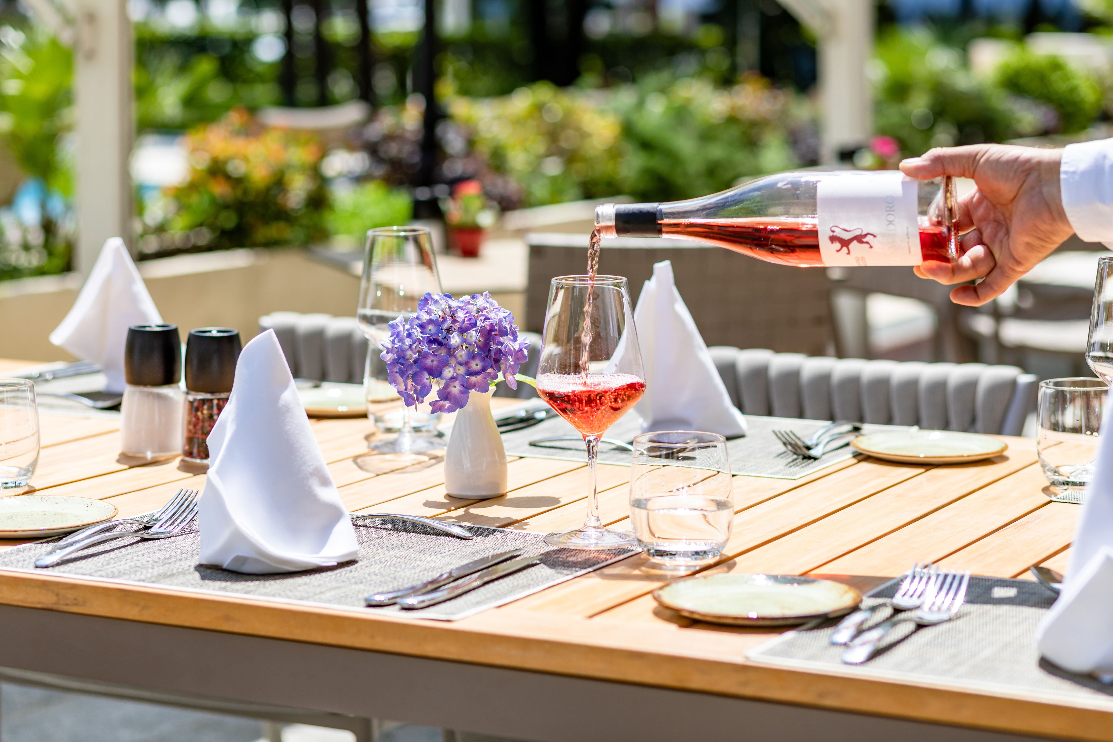 A table set for dining with a bottle of red wine being poured into a glass.