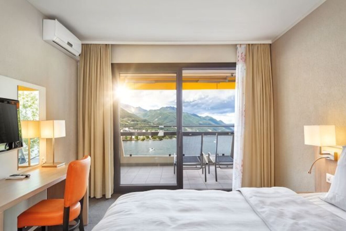 Habitación de hotel con cama, escritorio, silla, televisión y balcón con vistas a las montañas.