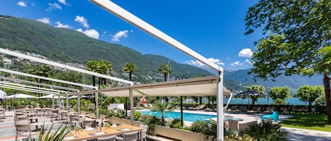 An outdoor dining area with tables and chairs, a pool, and a view of mountains and a lake.