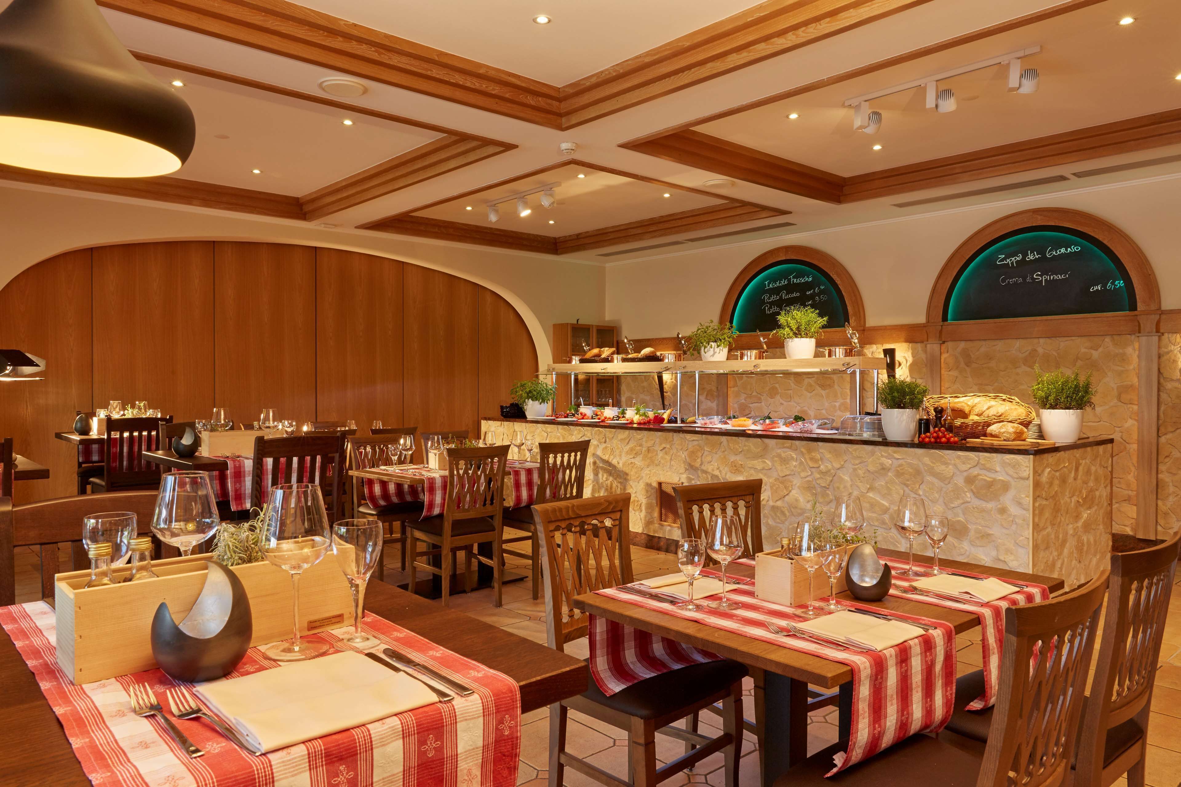 Un ristorante con travi a vista in legno, tavoli apparecchiati con bicchieri da vino e un'area buffet con un menu scritto su una lavagna.