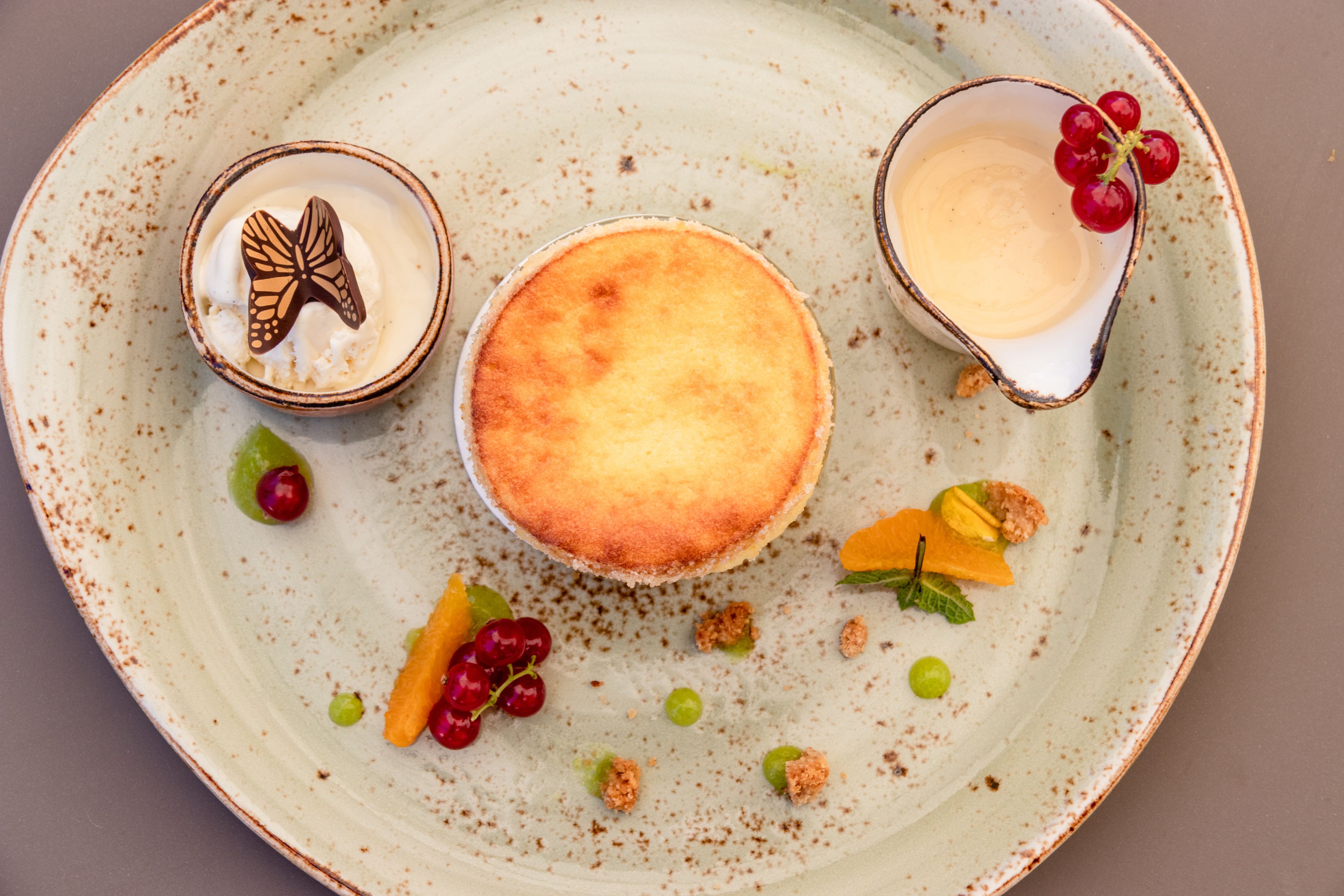 A dessert plate with a cheesecake, a small bowl with a butterfly decoration, and a glass with red grapes.