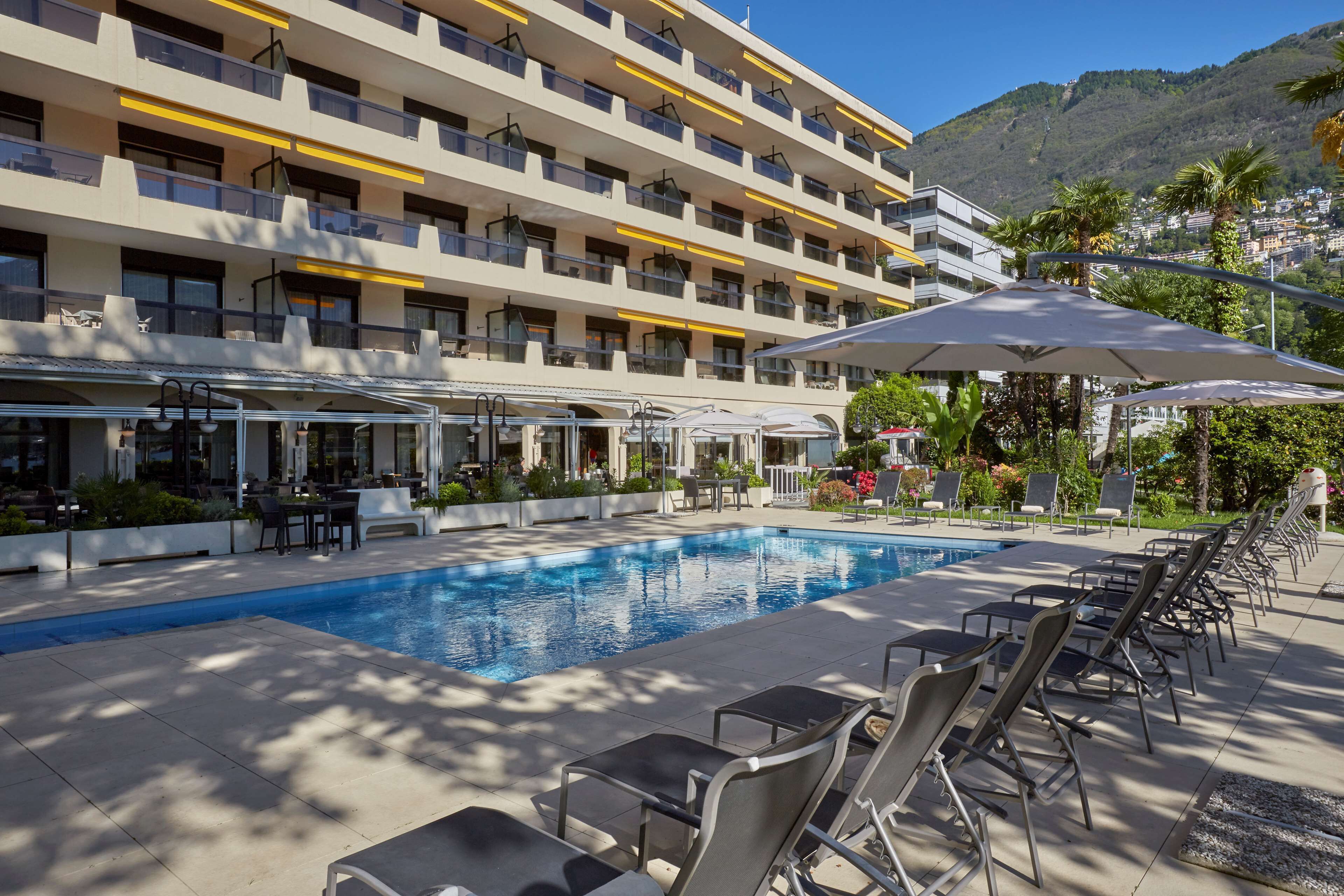 A hotel with a swimming pool, outdoor seating, and a mountain backdrop.