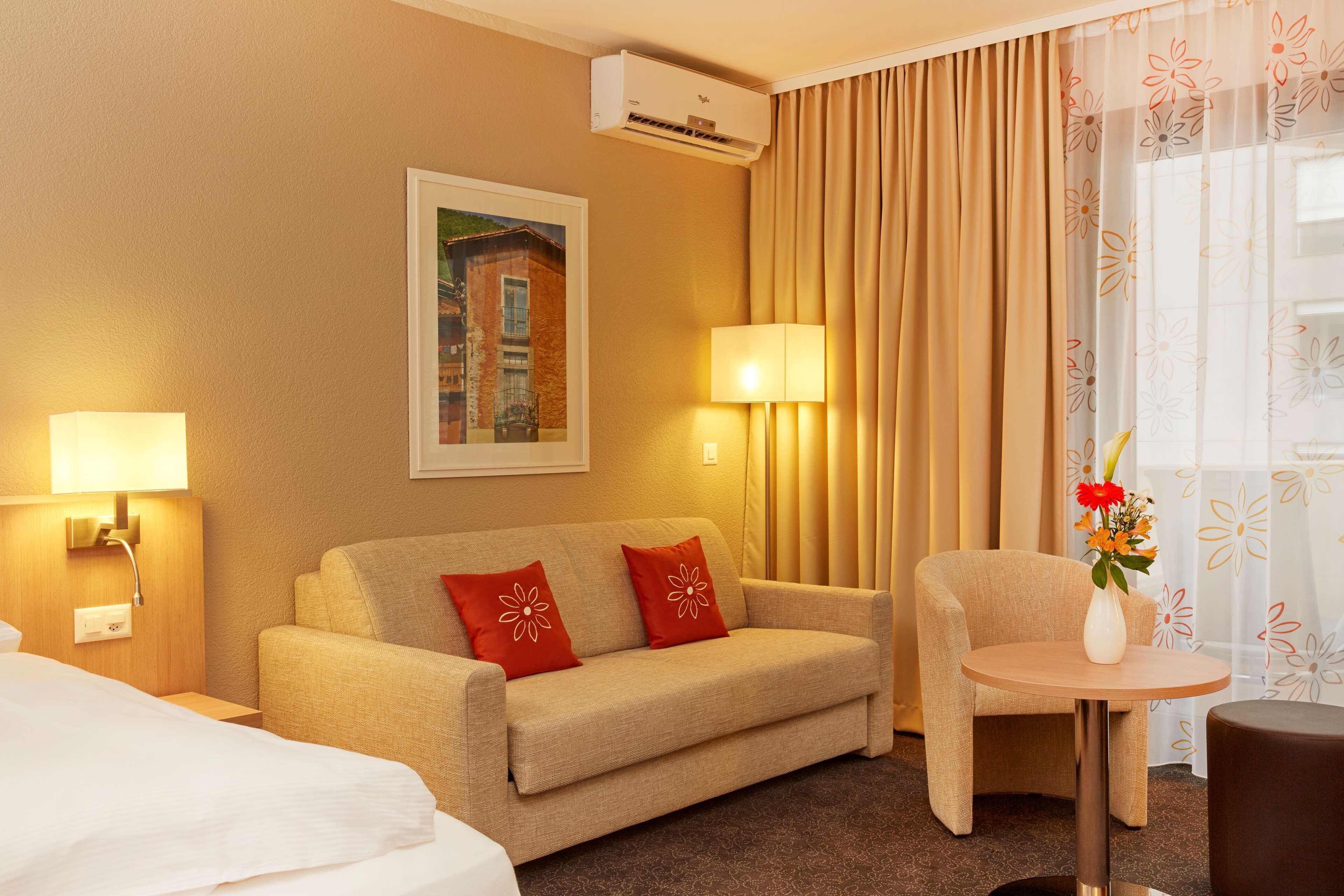 A hotel room with a sofa, a small round table, a lamp, and a painting on the wall.
