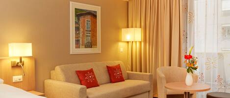A hotel room with a sofa, a small round table, a lamp, and a painting on the wall.