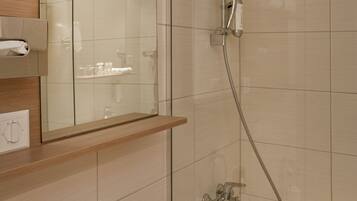 Un baño moderno con ducha de vidrio, inodoro integrado y espejo sobre un estante de madera.
