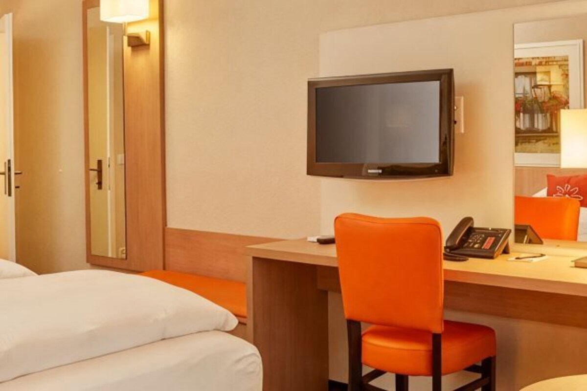 Una habitación de hotel con cama, escritorio, silla, televisor y teléfono.