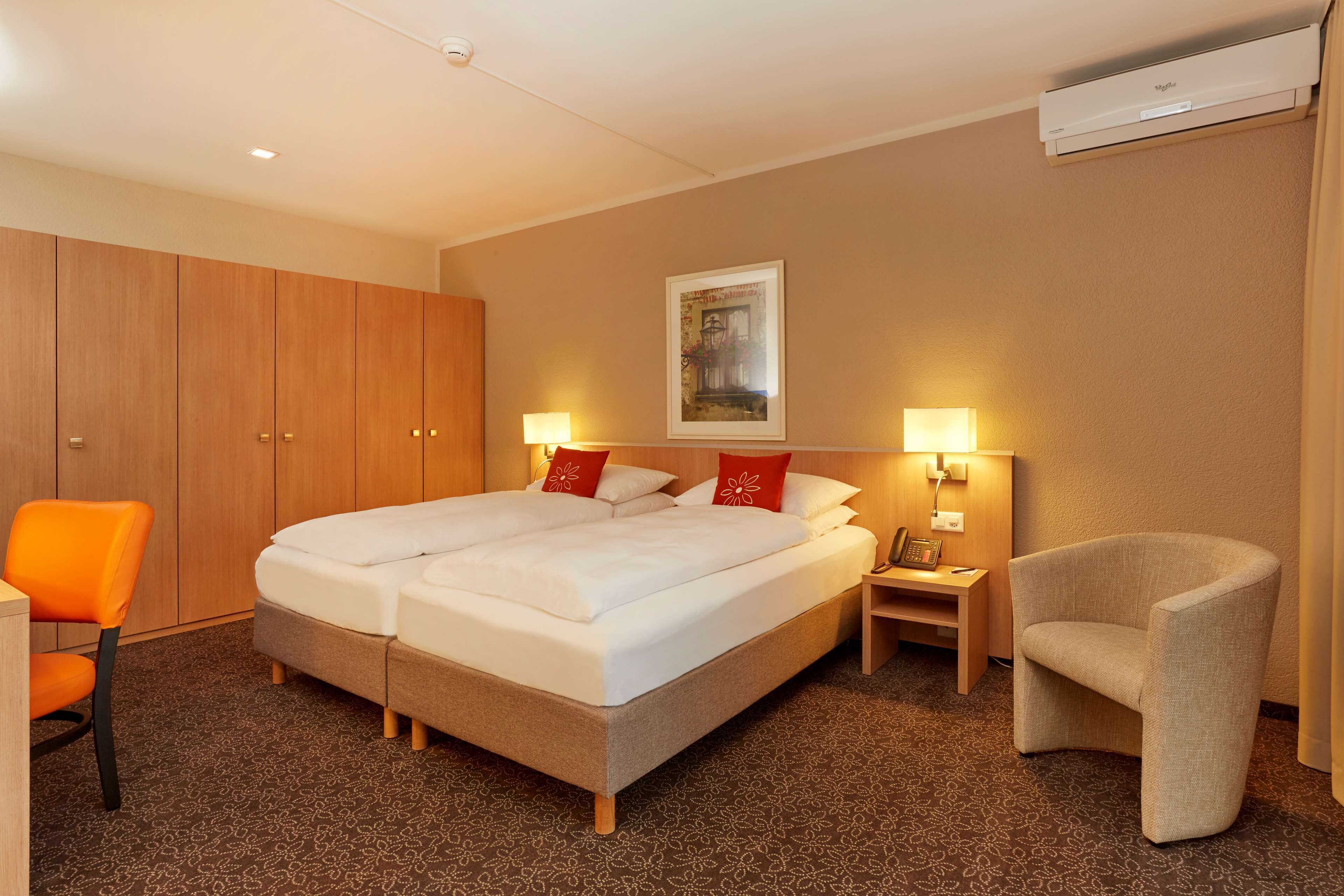 Una habitación de hotel con una cama grande, dos mesitas de noche, una silla, un escritorio y un armario.