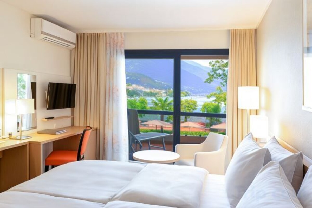 A hotel room with a bed, desk, chair, and a view of the outdoors.