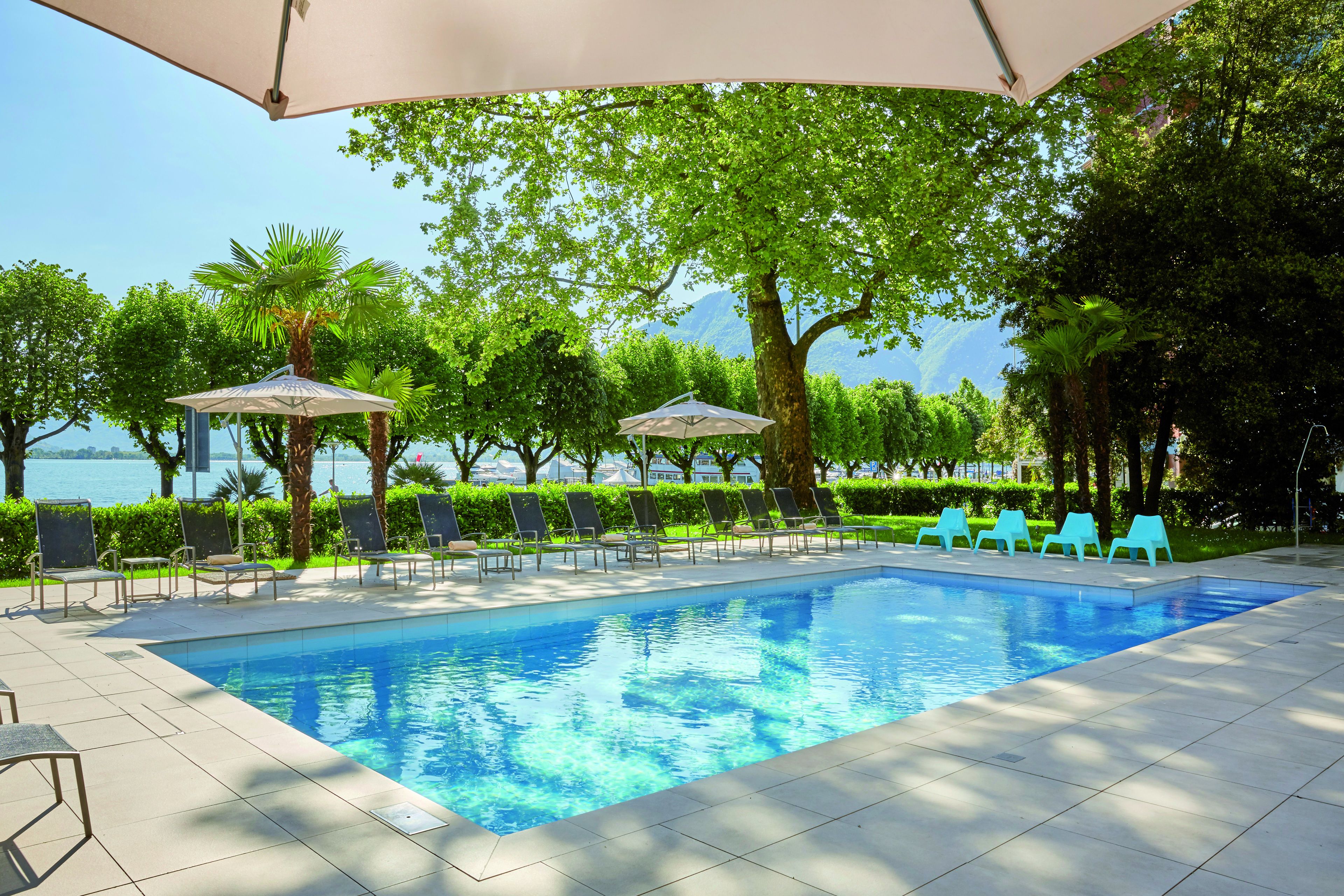 Una piscina con lettini e ombrelloni, immersa nel verde e con vista sull'acqua.