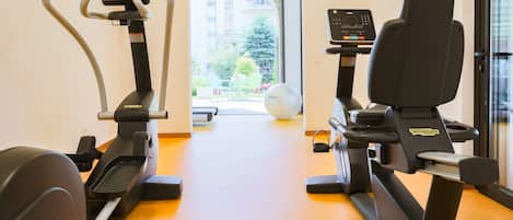 A gym with cardio machines and a view of a balcony with outdoor seating.