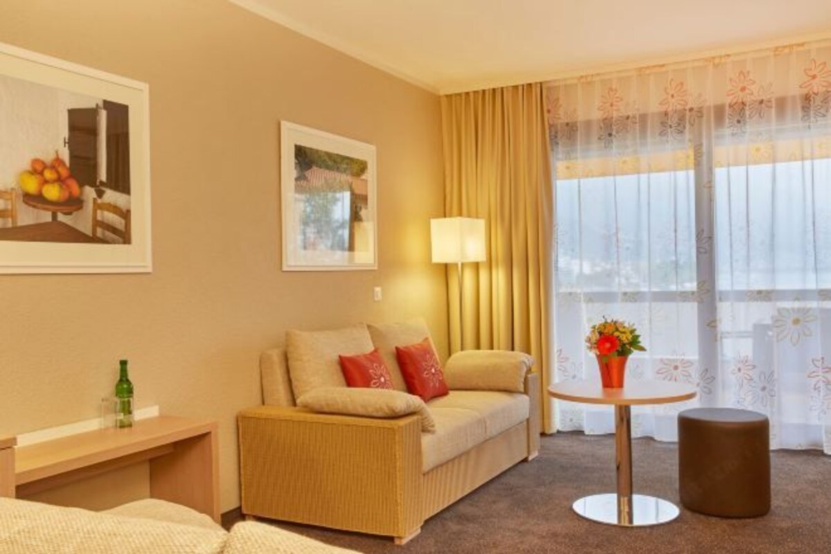 Une chambre d’hôtel avec un canapé, une petite table sur laquelle est posé un vase de fleurs, une lampe et un tableau au mur.