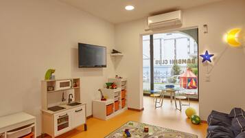 Cozy child-friendly room with a play area, kitchenette, and TV, offering a view of the outside.