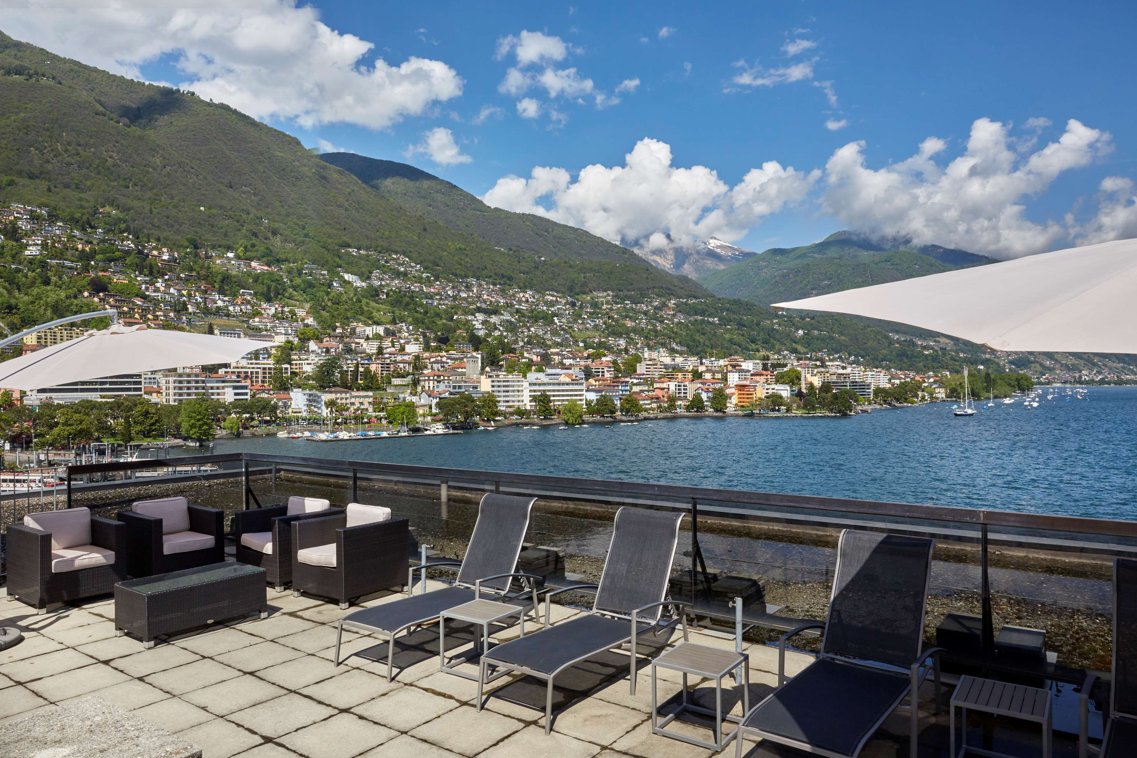 A terrace with outdoor seating overlooking a lake and a town.