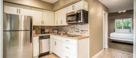 A modern kitchen with stainless steel appliances, white cabinetry, and a tiled backsplash.