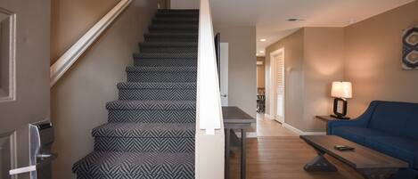 A staircase with patterned carpet, a wooden floor, a blue sofa, a table, and a lamp.