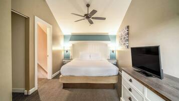 Una camera d'hotel con un letto, una televisione su una cassettiera in legno, una ventola a soffitto e due lampade da comodino.