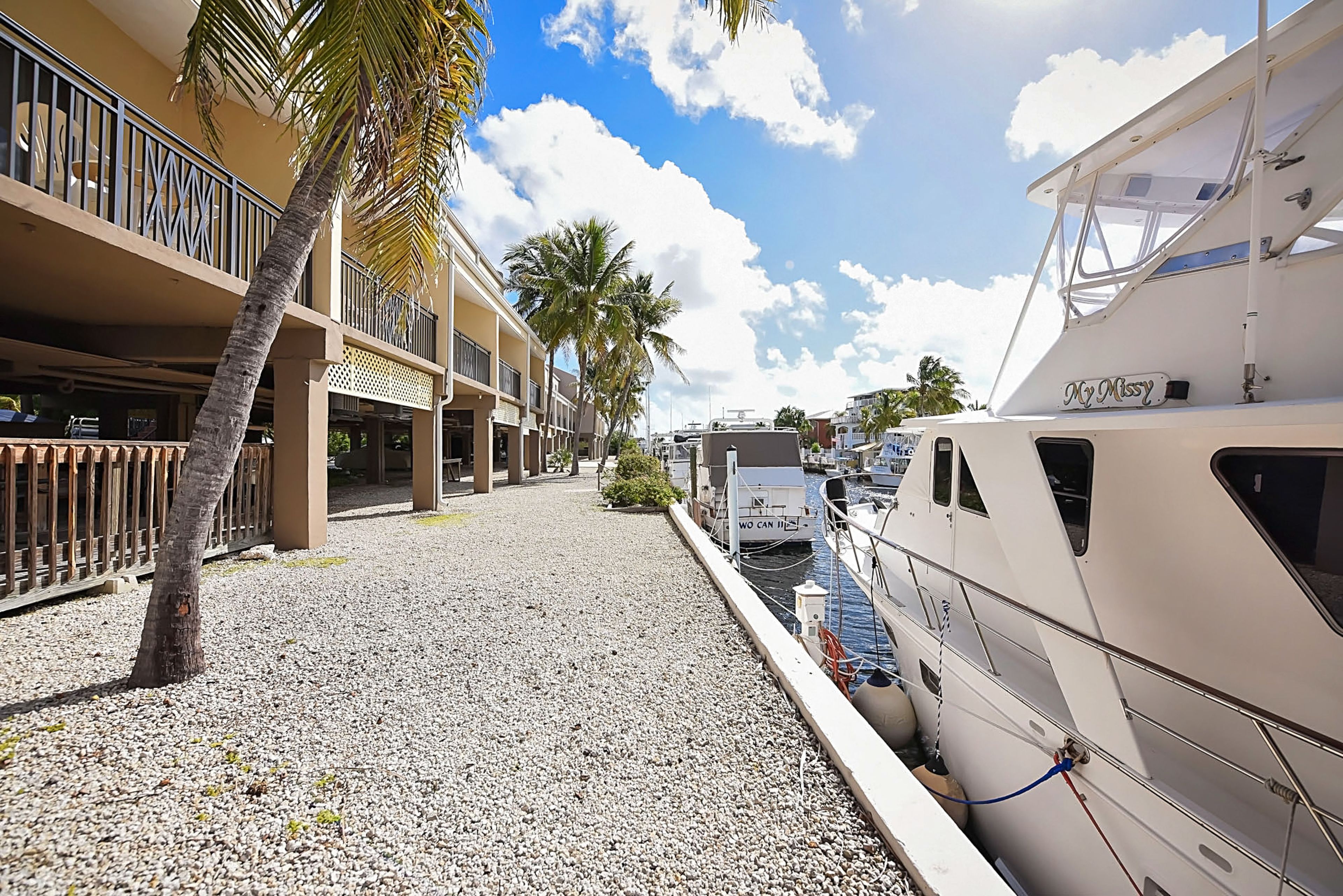 A marina with boats docked, a palm tree, and a building with balconies.