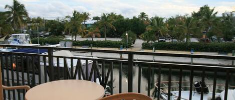 A balcony with a table and chairs, overlooking a marina with boats and palm trees.