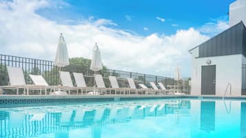 Una piscina al aire libre, sombrillas, sillones reclinables de piscina