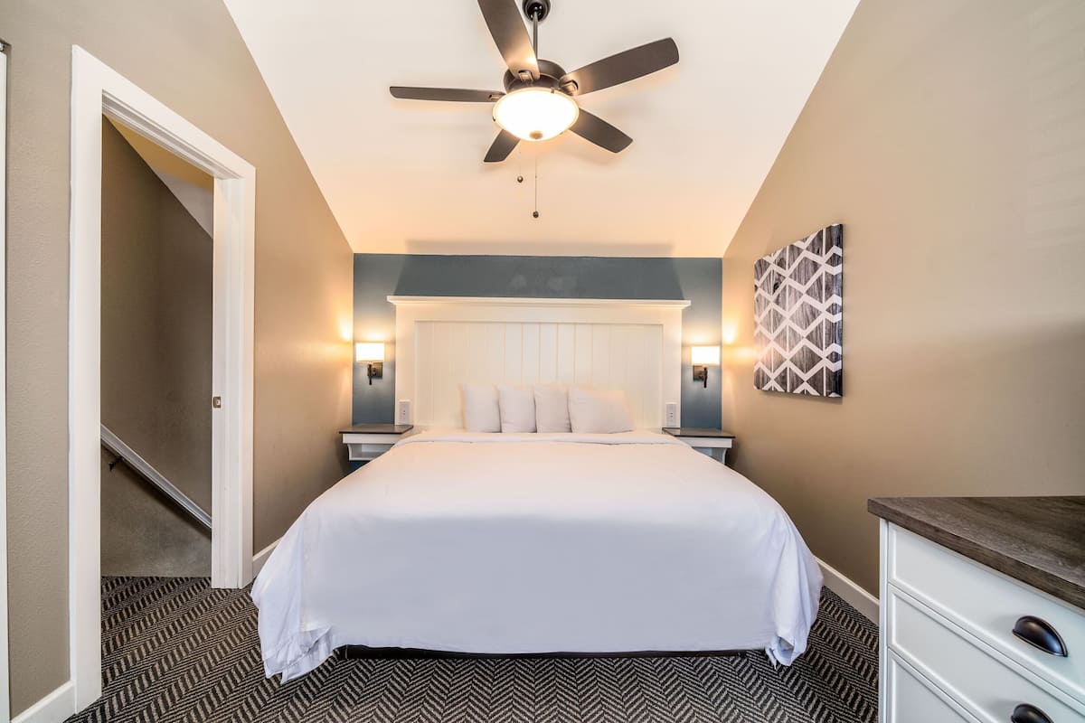 A bedroom with a bed, a ceiling fan, a nightstand, a dresser, and a wall-mounted artwork.
