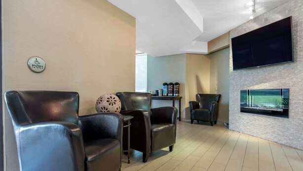A modern hotel lobby with leather armchairs, a flat-screen TV mounted on the wall, and a fireplace.