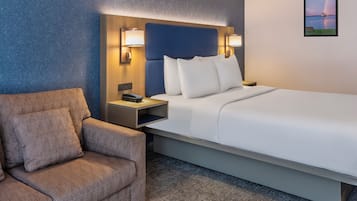 Quarto de hotel com cama, cadeira, mesa de cabeceira e luminária na parede.
