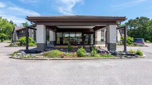 A modern building with a covered entrance, large windows, and a landscaped garden area.