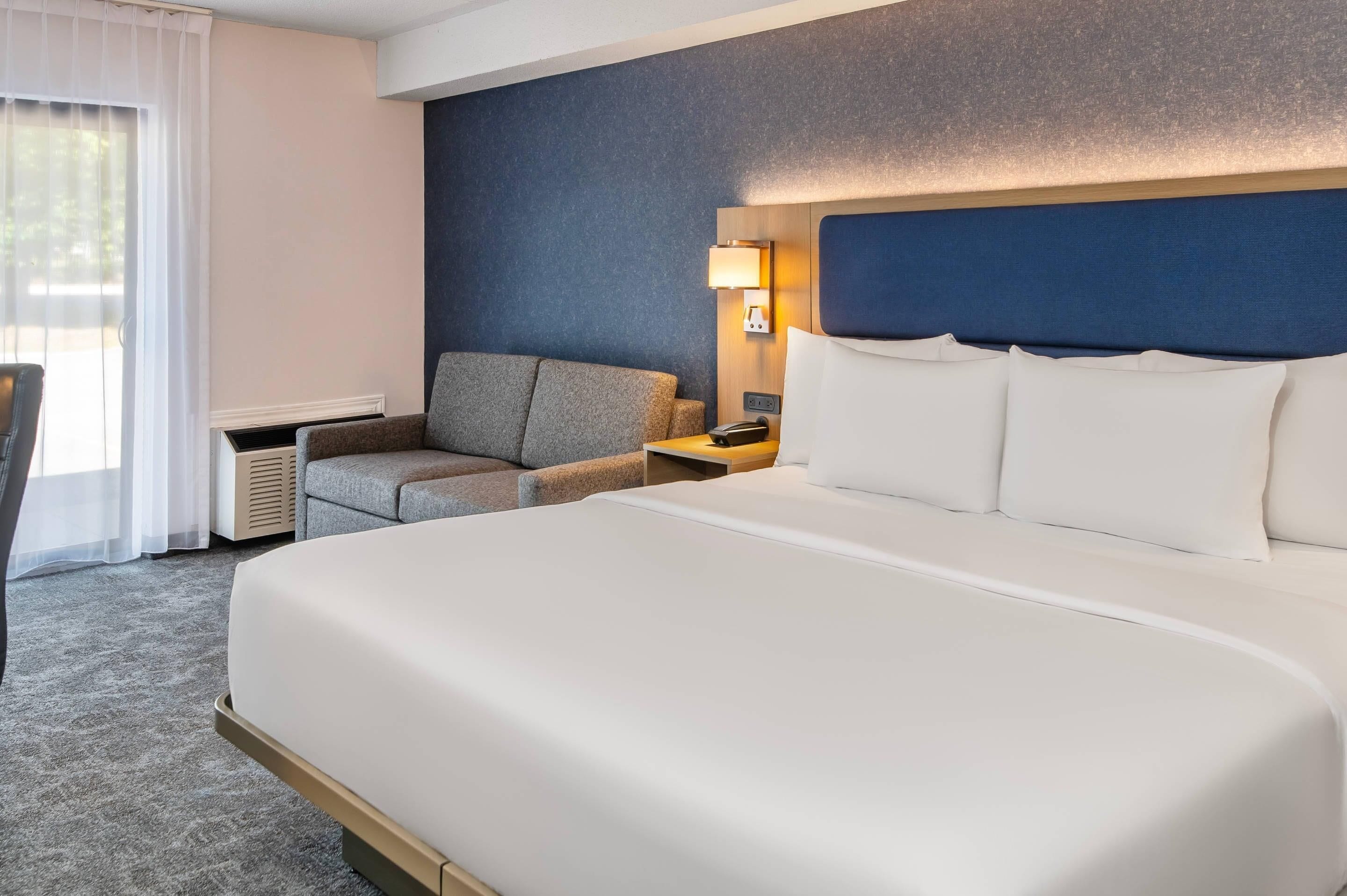 A hotel room with a large bed, a desk, a chair, and a nightstand.