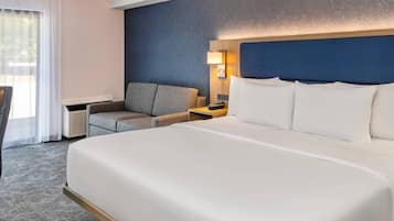 A hotel room with a large bed, a desk, a chair, and a nightstand.