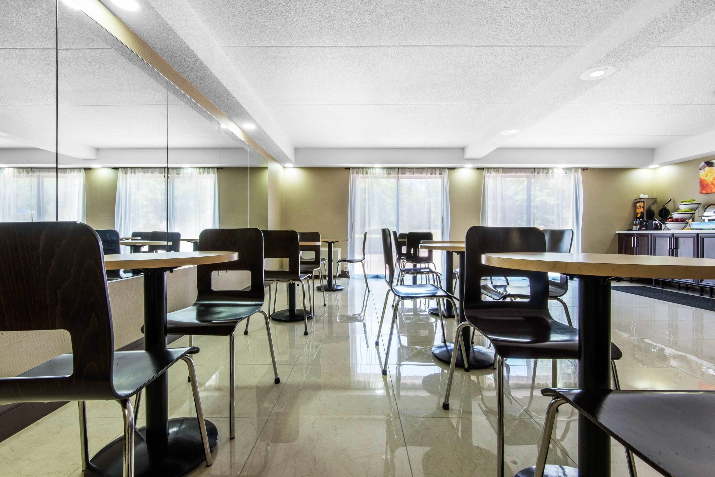A modern dining area with tables and chairs, large windows with curtains, and a clean, tiled floor.