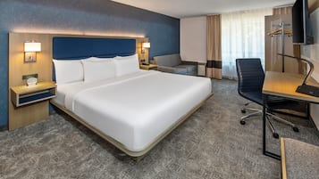 A hotel room with a large bed, a desk with a chair, a TV, and a window with curtains.