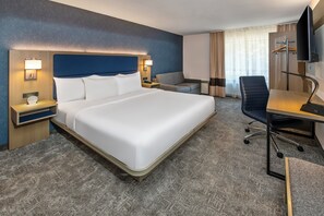 A hotel room with a large bed, a desk with a chair, a TV, and a window with curtains. - Comfort Inn (North Bay)