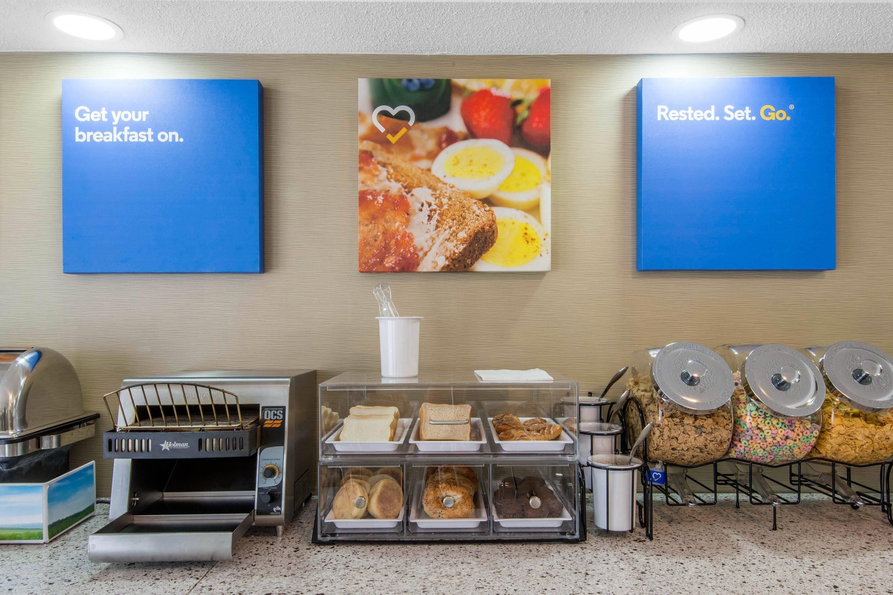 A breakfast area with a coffee machine, bread, pastries, and cereal containers.