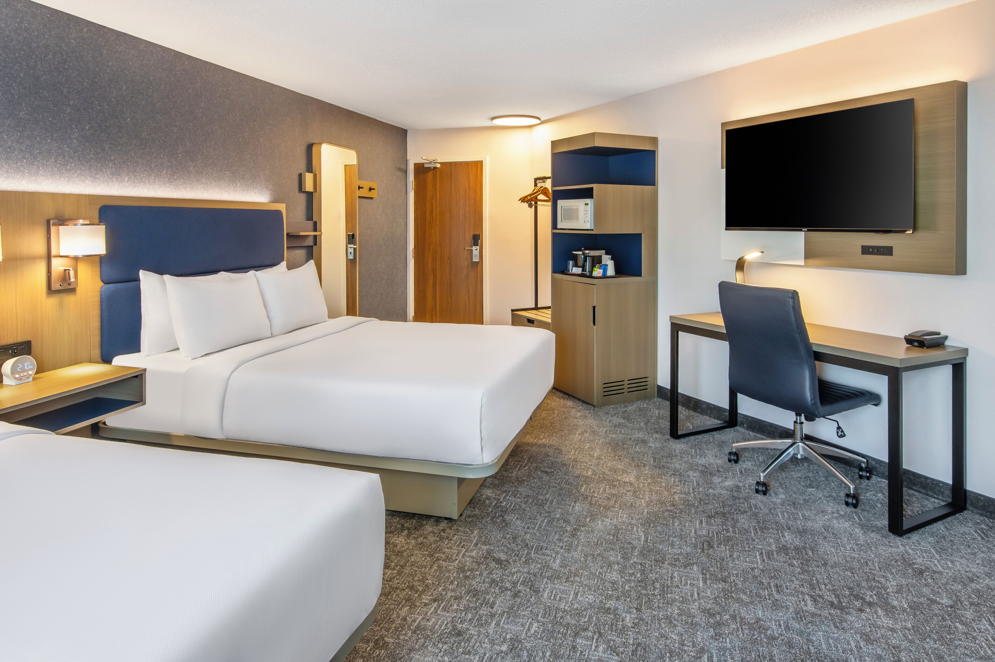 Una habitación de hotel con cama, escritorio, silla, televisor y armario.