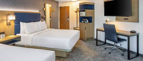 Una habitación de hotel con cama, escritorio, silla, televisor y armario.