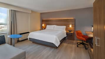 A hotel room with a bed, bedside table, chair, desk, and wardrobe.