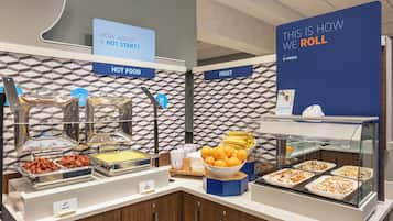 A buffet setup with labeled sections for hot food, fruit, and a roll station.